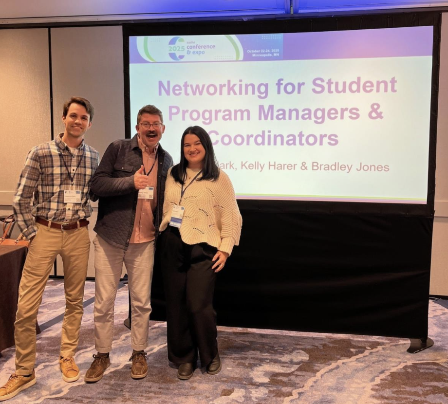 Three people stand next to a presentation screen that says 